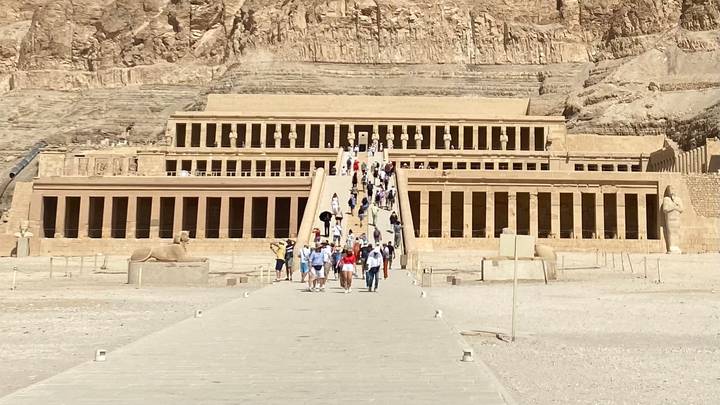 Visitors ascend the grand ramp to the terraced Temple of Hatshepsut carved into desert cliffs.