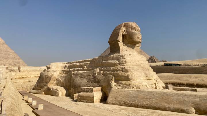 The Great Sphinx of Giza in the desert with pyramids and hazy sky behind.