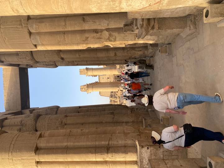 Tourists walk between towering decorated columns in Luxor Temple’s colonnade.