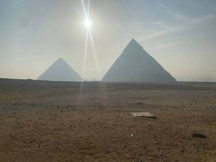 Misty sunrise over the desert with silhouettes of the pyramids and sun rays cutting through the haze.