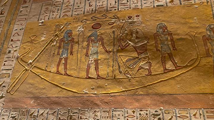 Colorful painted relief of ancient Egyptian figures on a tomb wall surrounded by hieroglyphs.