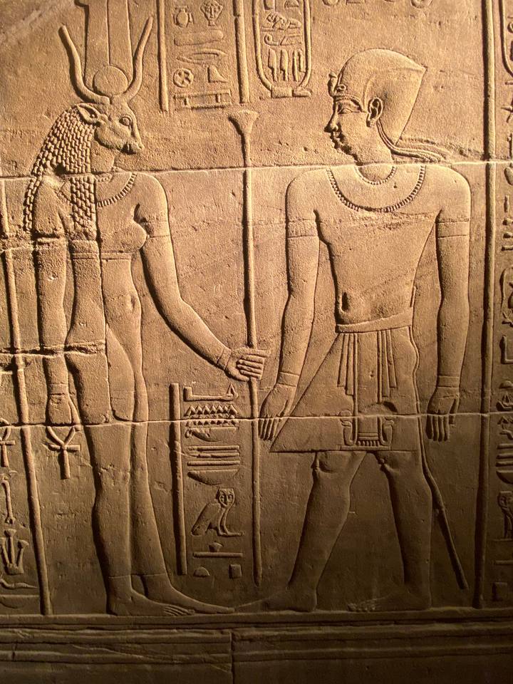 Close-up of finely carved stone hieroglyphs and figures illuminated by warm light.