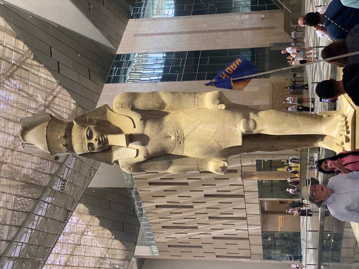 Massive ancient statue of a pharaoh inside the Grand Egyptian Museum atrium with visitors standing below.