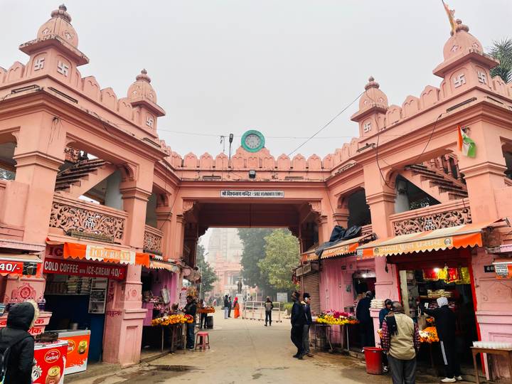 A pink arched gateway bustles with locals buying flowers and snacks beneath a hazy sky.