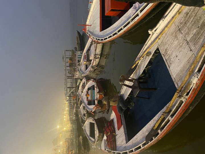 Wooden rowboats wait at a misty dock in evening light while a lone man sits aboard.