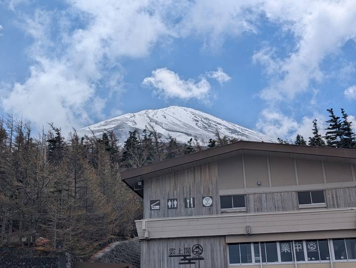 Snow-capped Mount Fuji rising above forested slopes and a wooden visitor building