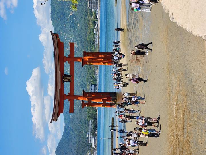 Crowds gather around the towering vermilion torii gate of Itsukushima Shrine at low tide