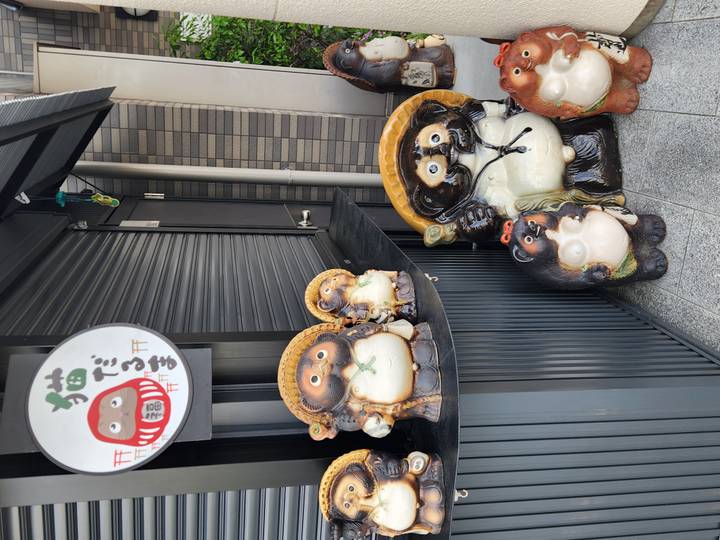 Row of whimsical ceramic tanuki statues outside a shuttered Japanese storefront