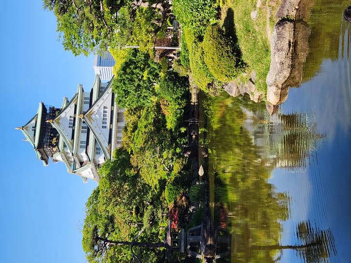 Osaka Castle rising above manicured gardens with perfect reflection in a pond