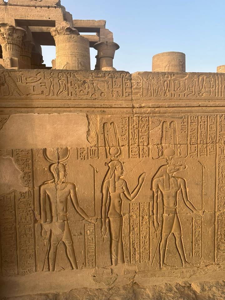 Detailed ancient Egyptian relief carvings depicting deities and hieroglyphs on a sandstone temple wall.