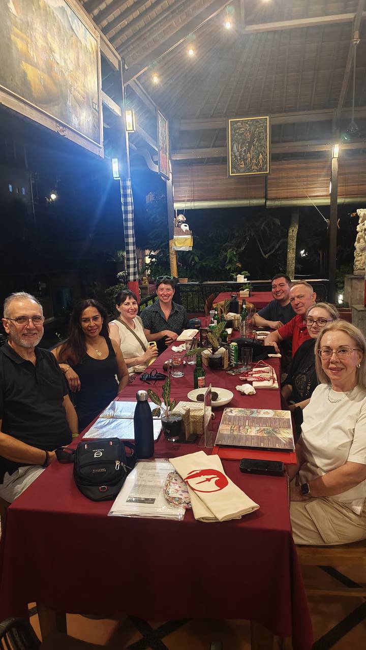 Tour group seated around dinner table at outdoor restaurant at night in Bali.
