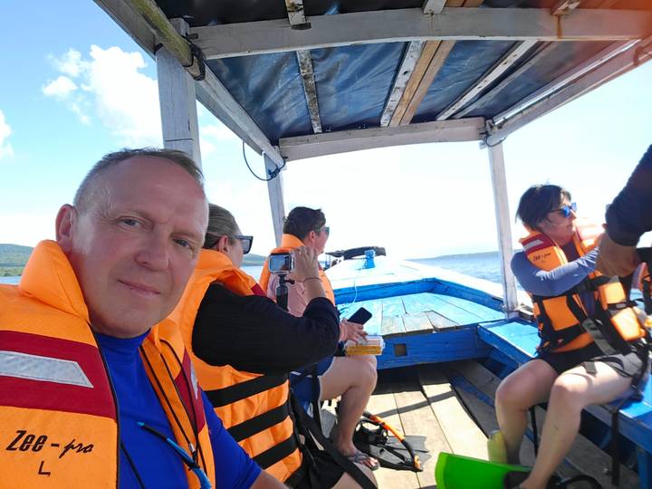Travelers wearing orange life jackets riding in small wooden boat on blue sea.