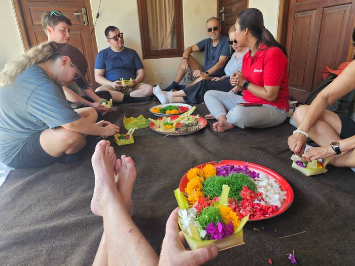 Group seated on floor crafting colorful Balinese offerings with flowers and leaves.