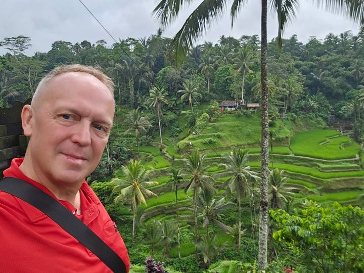 Traveler taking a selfie overlooking lush green terraced rice paddies and tall palm trees in Bali.
