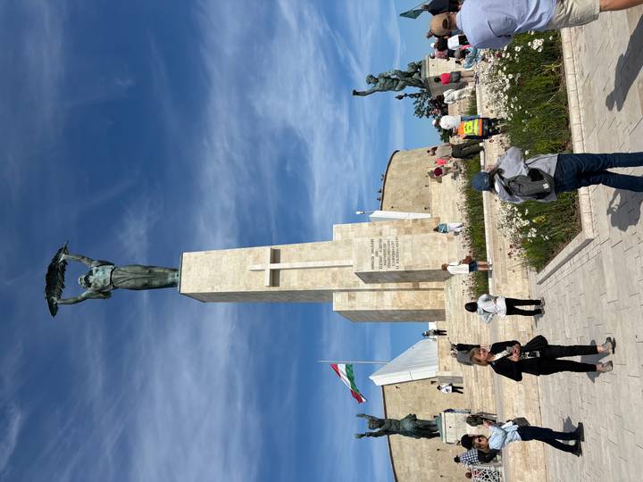 Visitors at a tall liberty statue atop stone pedestal with national flag waving