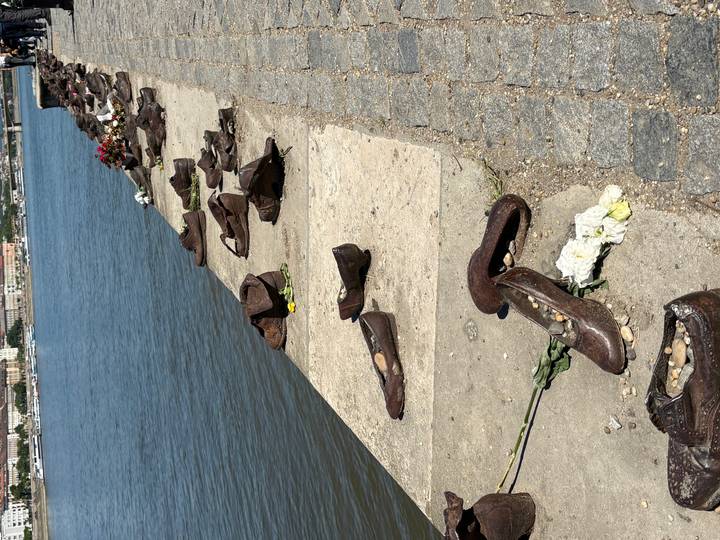 Bronze shoes memorial lining a stone quay along a calm river under bright sun