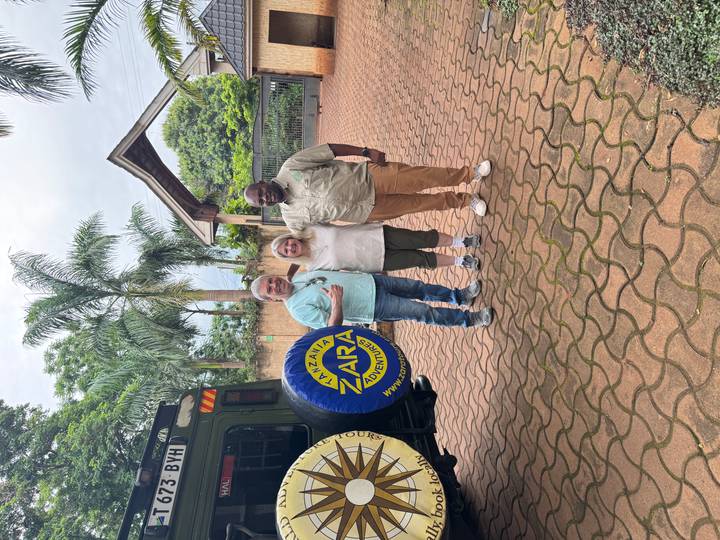 Two travellers posing with their safari guide beside a green 4x4 in a lodge courtyard