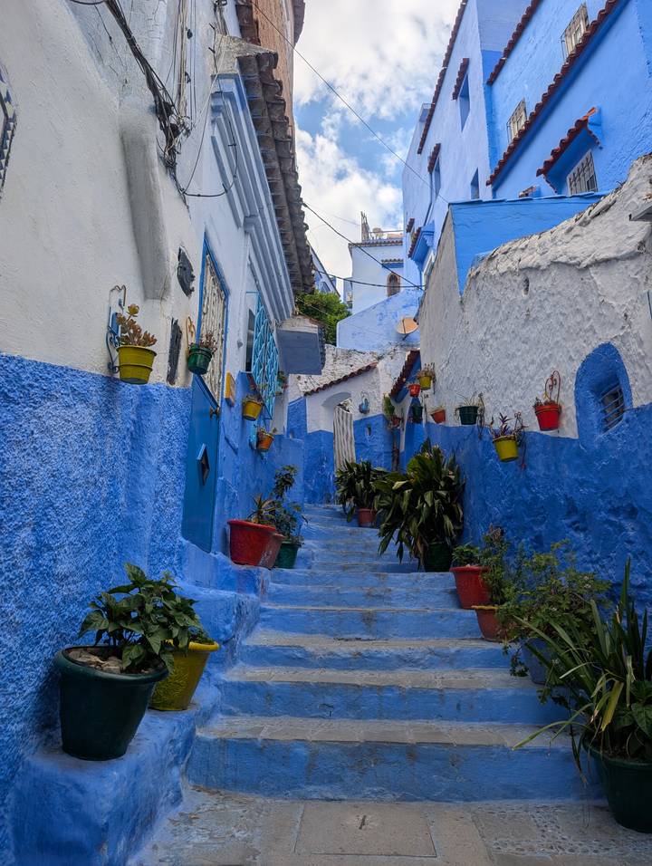 A steep alley of blue-washed walls and colorful flower pots climbs upward in Chefchaouen’s medina.