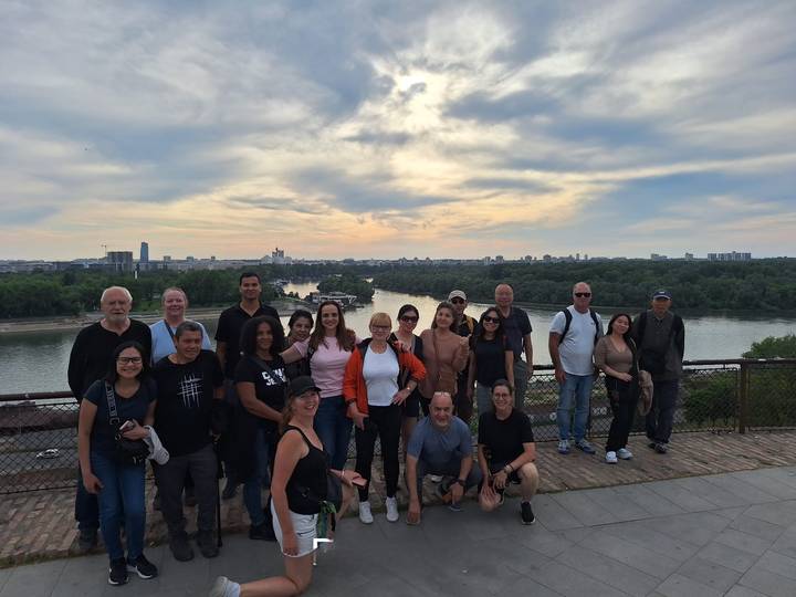 Large tour group posing on a fortress terrace overlooking the confluence of two rivers at sunset.