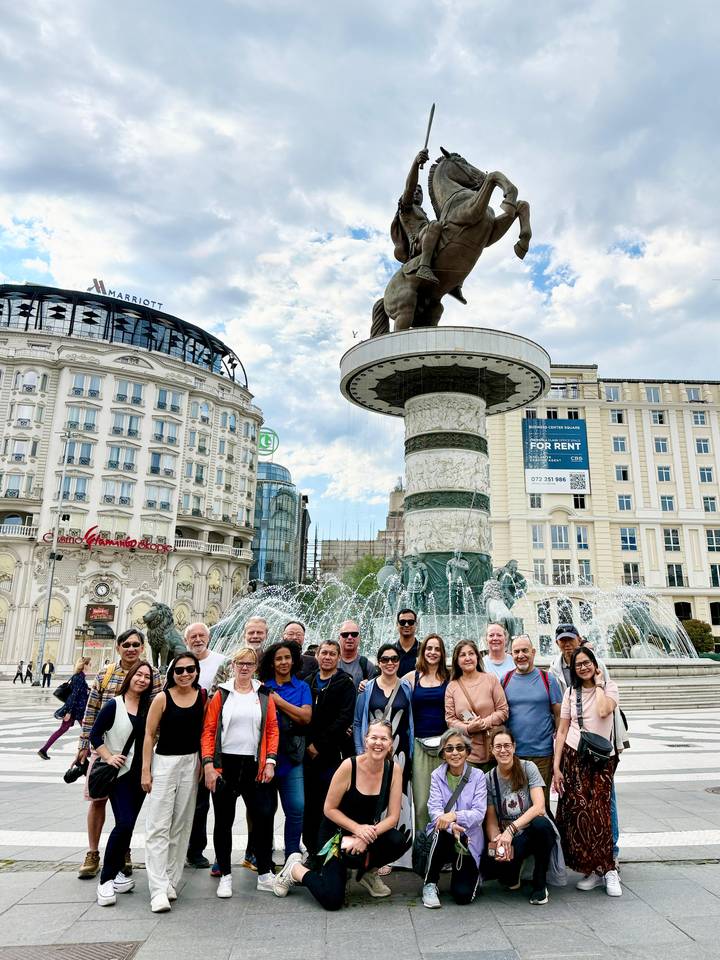Closer shot of the same group in front of Skopje’s ornate fountain with water jets framing them.