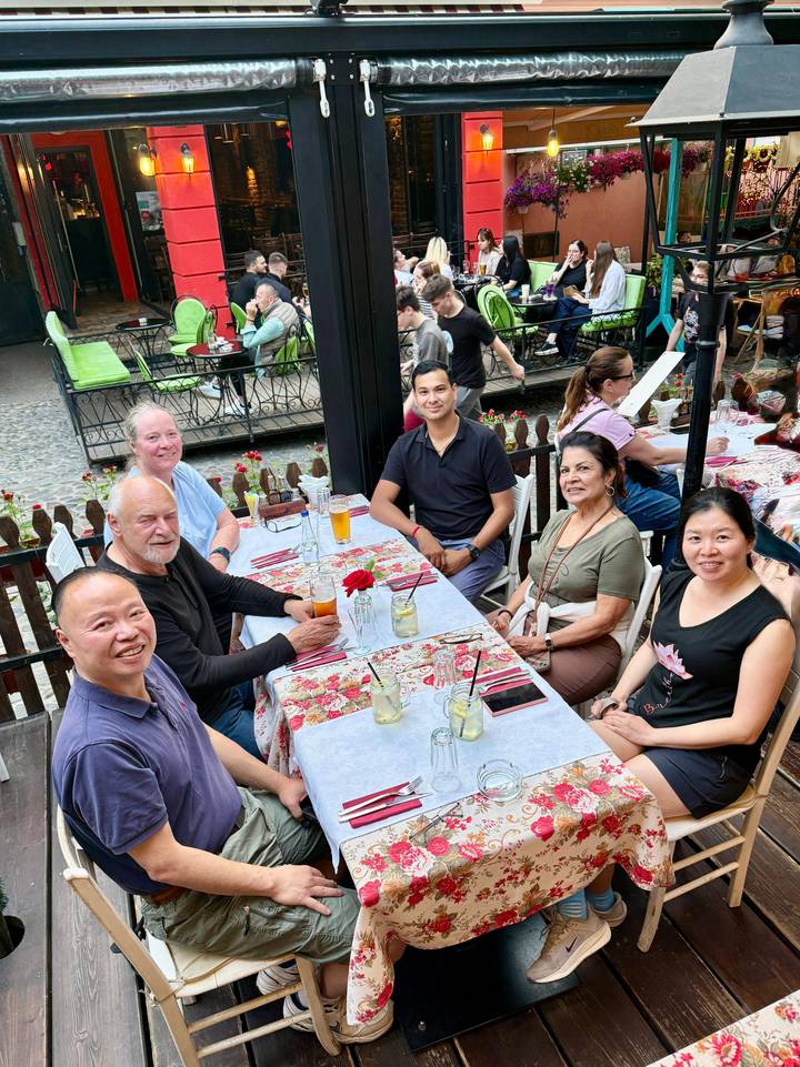 Small group enjoying drinks at an outdoor riverside café with cobblestone setting.