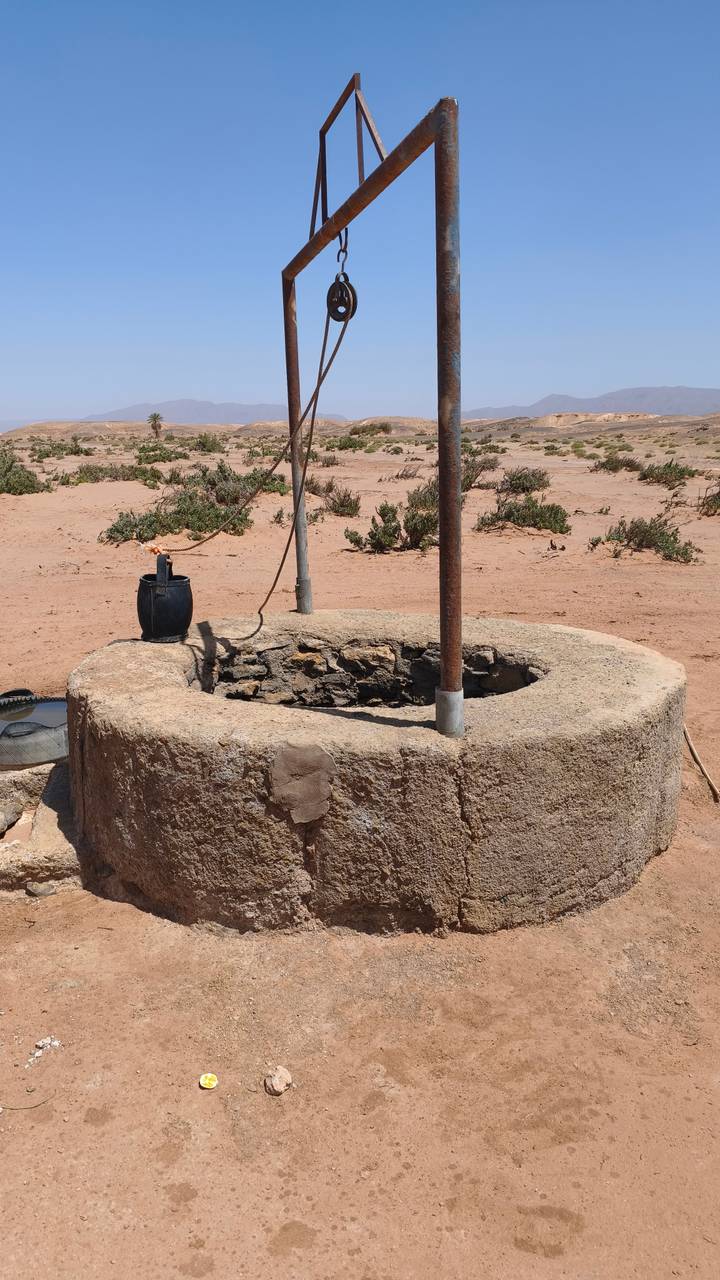 Old stone well with bucket in a barren desert landscape.