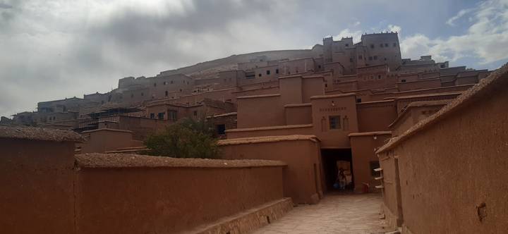 Earthen ramparts and stacked clay buildings of an ancient kasbah rise beneath a cloudy sky.