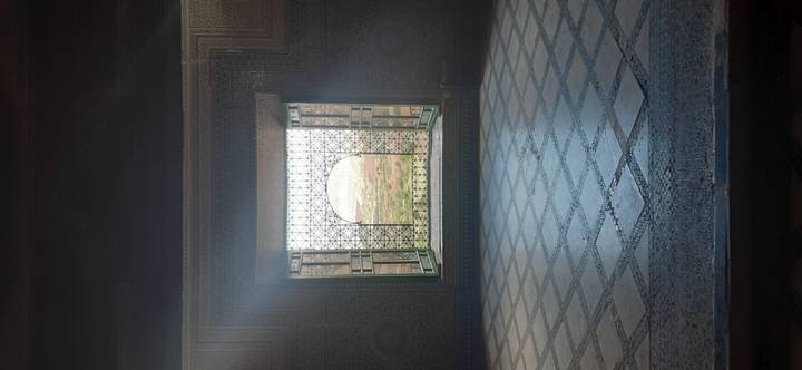 Mosaic-framed arched window inside an ornate palace room looks out onto gardens and distant cityscape.