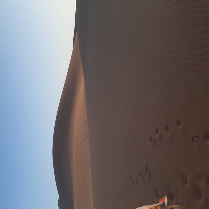 Smooth brown sand dune with a single line of footprints leading into the distance beneath clear dawn sky.