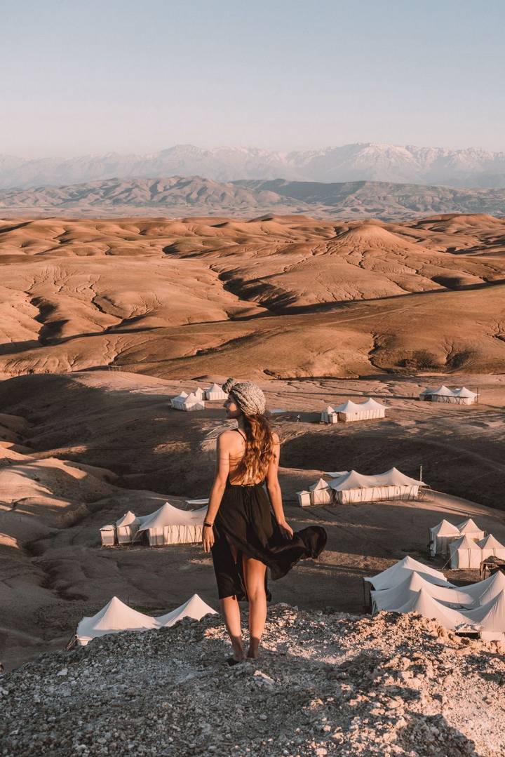 Young woman gazes over remote desert camp of white canvas tents scattered across rolling tan hills.