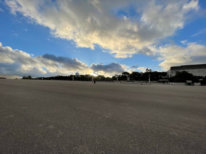 Vast paved esplanade under dramatic evening clouds with the sun breaking at the horizon.