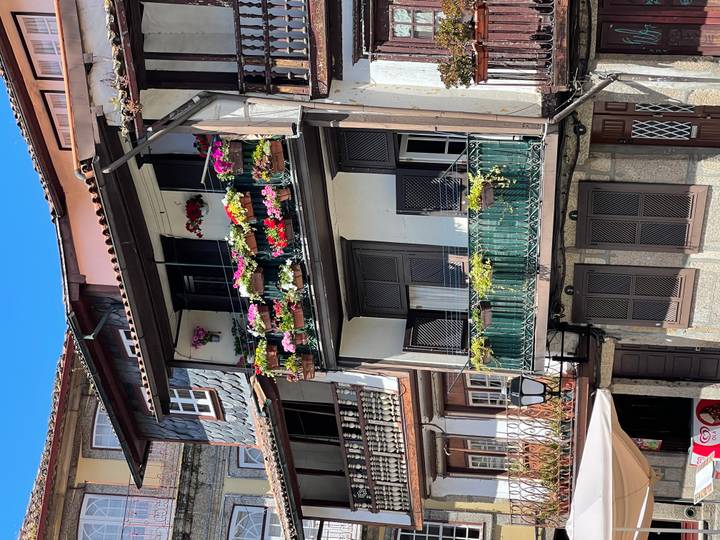 Traditional Portuguese townhouse façade with balconies overflowing with colourful flowers against clear sky.
