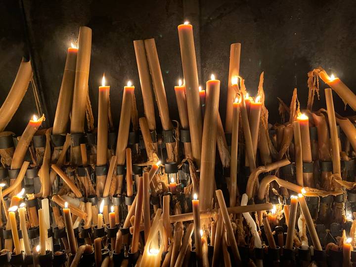 Cluster of lit devotional candles melting inside a dim chapel.