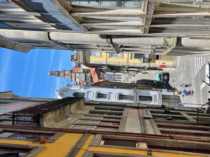 Narrow Porto alley framing Clerigos Tower at the end, with bright façades and small figures below.