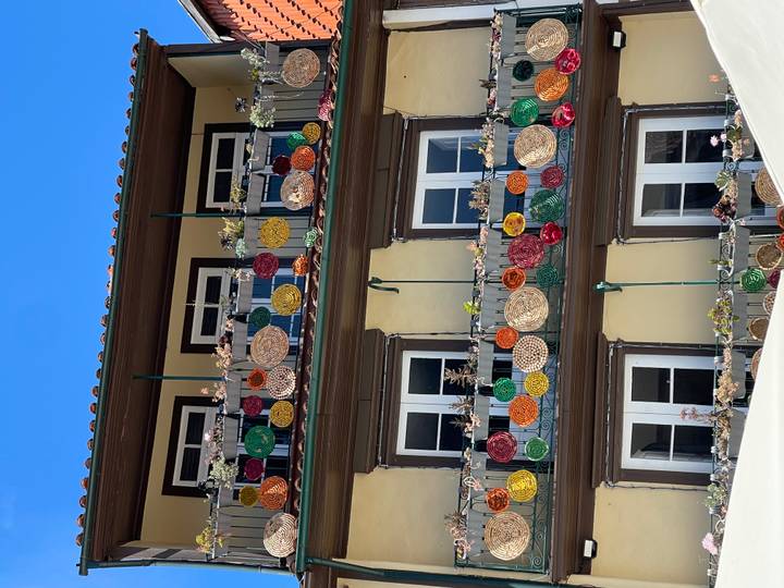 Building with three balconies decorated by colourful woven baskets and succulents against a bright sky.