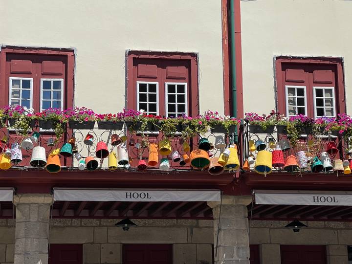 Row of balconies festooned with colourful hanging pots and flowers on a historic Portuguese arcade.