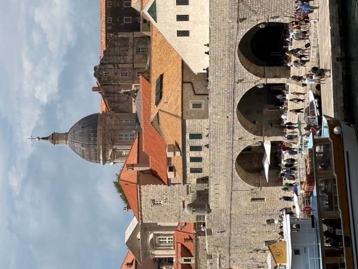 Dubrovnik harbour scene with arched stone warehouses, cathedral dome and boats moored in front.