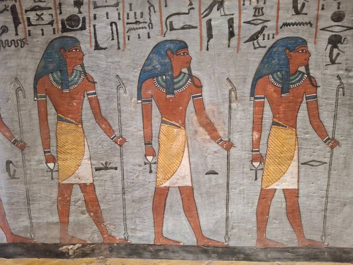 Ancient Egyptian wall painting of three male figures in traditional dress holding staffs.