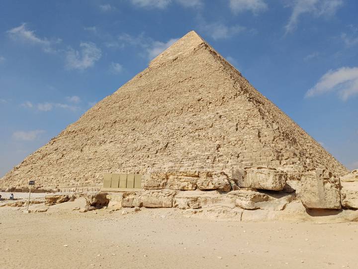 Great Pyramid of Giza soaring into blue sky with weathered limestone blocks in foreground.