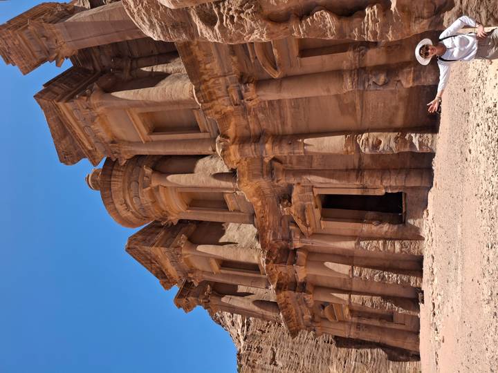 Sandstone façade of Petra Monastery towering above visitor’s outstretched arm.