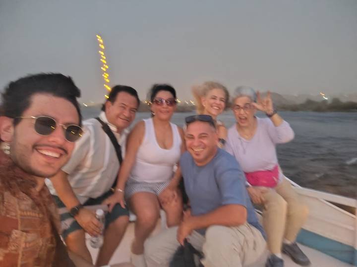 Blurry dusk selfie of six travelers laughing on a small Nile boat with festive lights