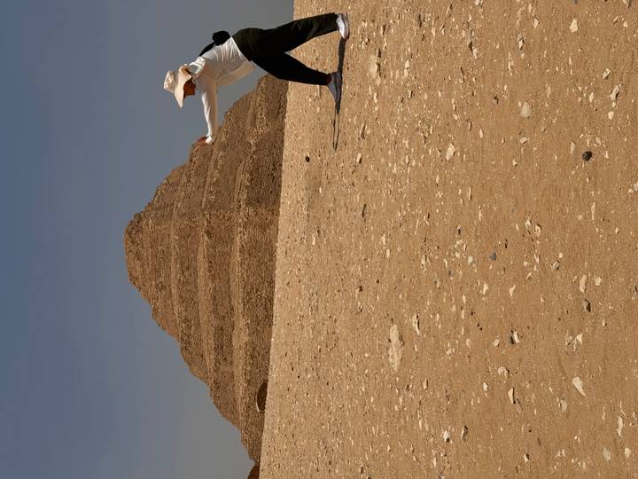 Visitor playfully posing before the Step Pyramid of Djoser on a sandy plateau