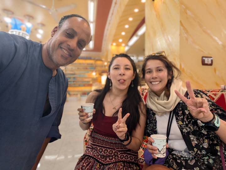 Three friends share cups of tea, flashing peace signs in a brightly lit shop interior.