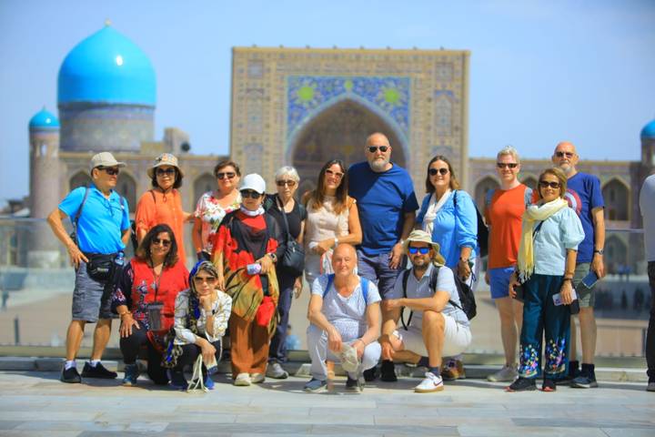 Large tour group posing on a terrace with the ornate Registan madrasa complex blurred in the background