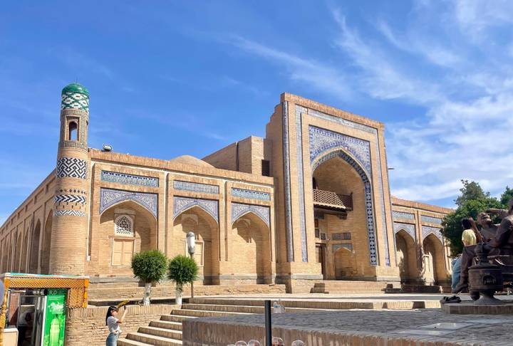 Historic brick mosque with ornate blue-tile arches and a slender green-topped minaret under a clear blue sky.
