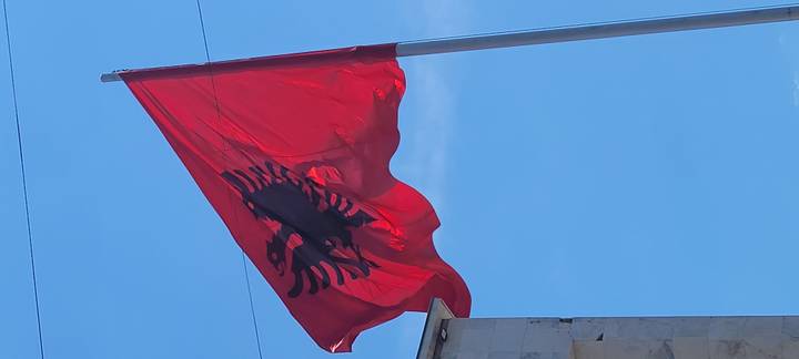 Bright red Albanian flag with black double-headed eagle waving against clear blue sky