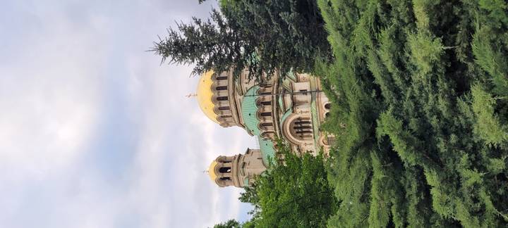 Golden-domed Alexander Nevsky Cathedral rising above lush greenery under soft clouds