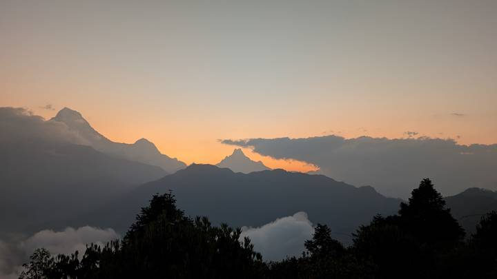 Serene Himalayan peaks silhouetted against a pastel sunrise with low clouds in the valleys.