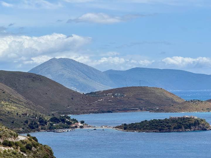 Blue coastal inlet surrounded by green and brown rolling hills with layered mountain backdrop.