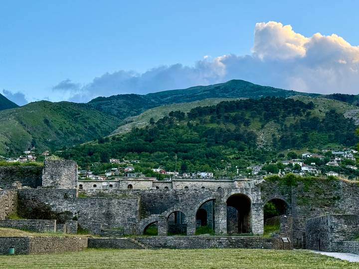 Stone walls and arches of Gjirokastra Castle set against green mountains at dusk.